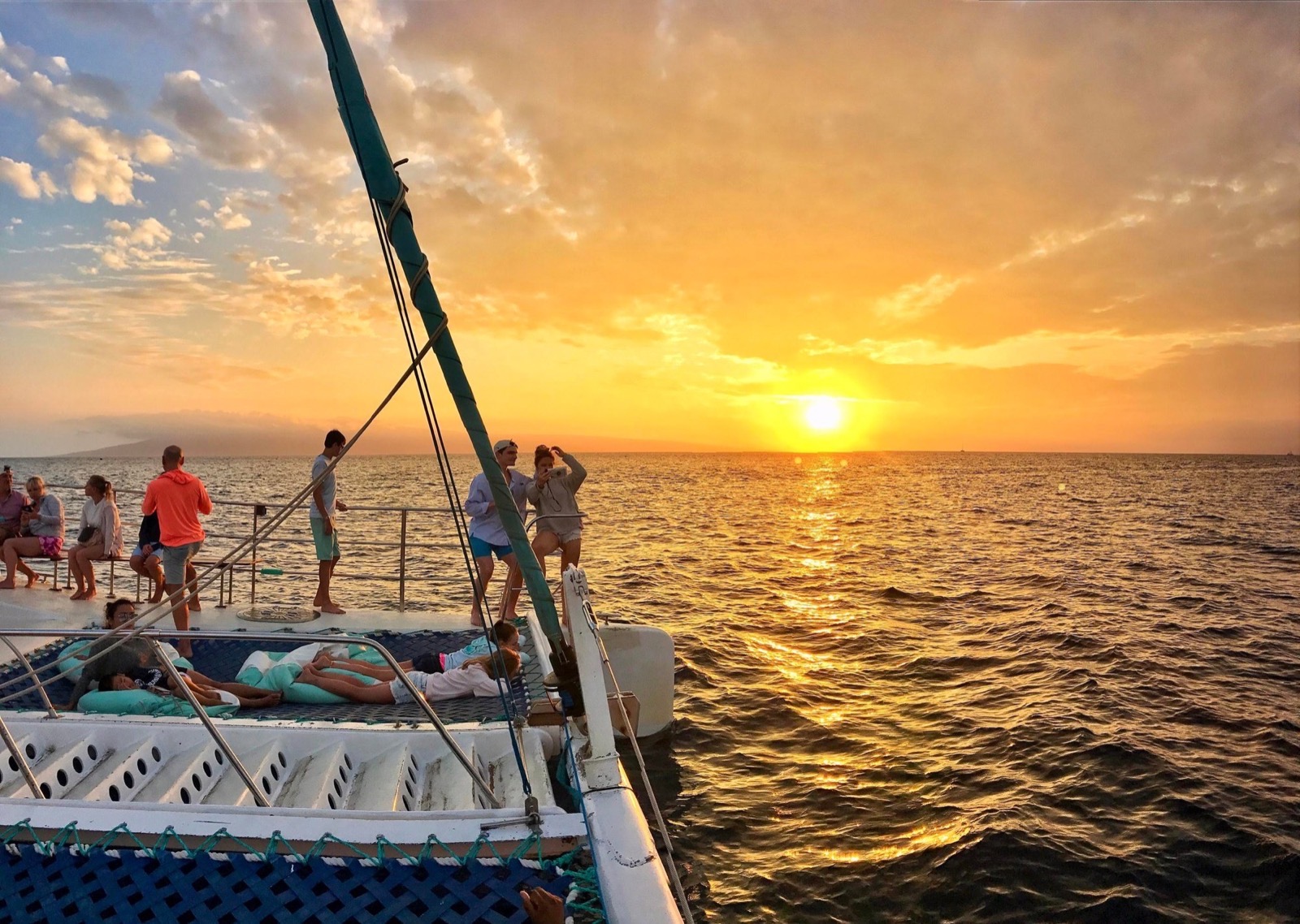 Guests relaxing on the catamaran trampoline and deck as a golden sun sets over the Pacific