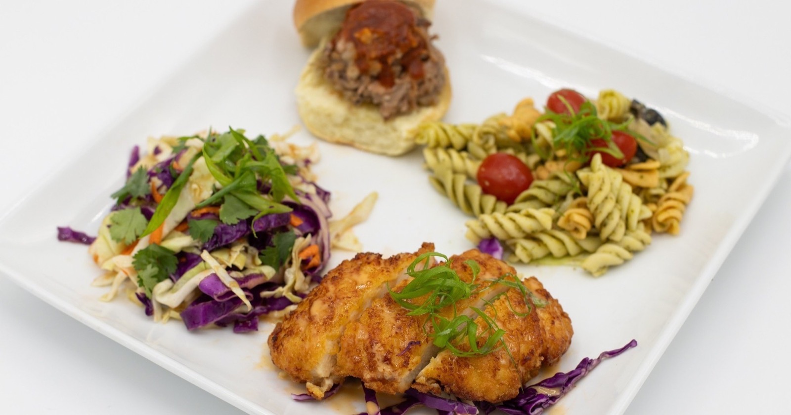 Plate of pupus with a pulled pork slider, pesto pasta salad, Asian slaw and sliced fried chicken