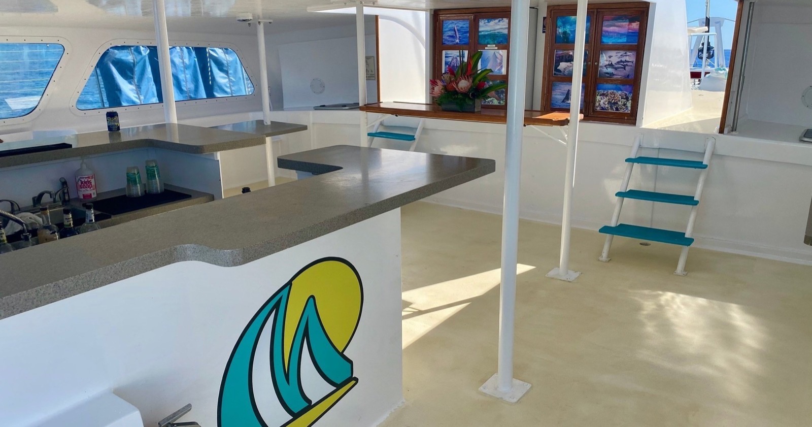 Inside the catamaran cabin, the open bar counter with the Sea Maui logo, bench seating and framed marine photos