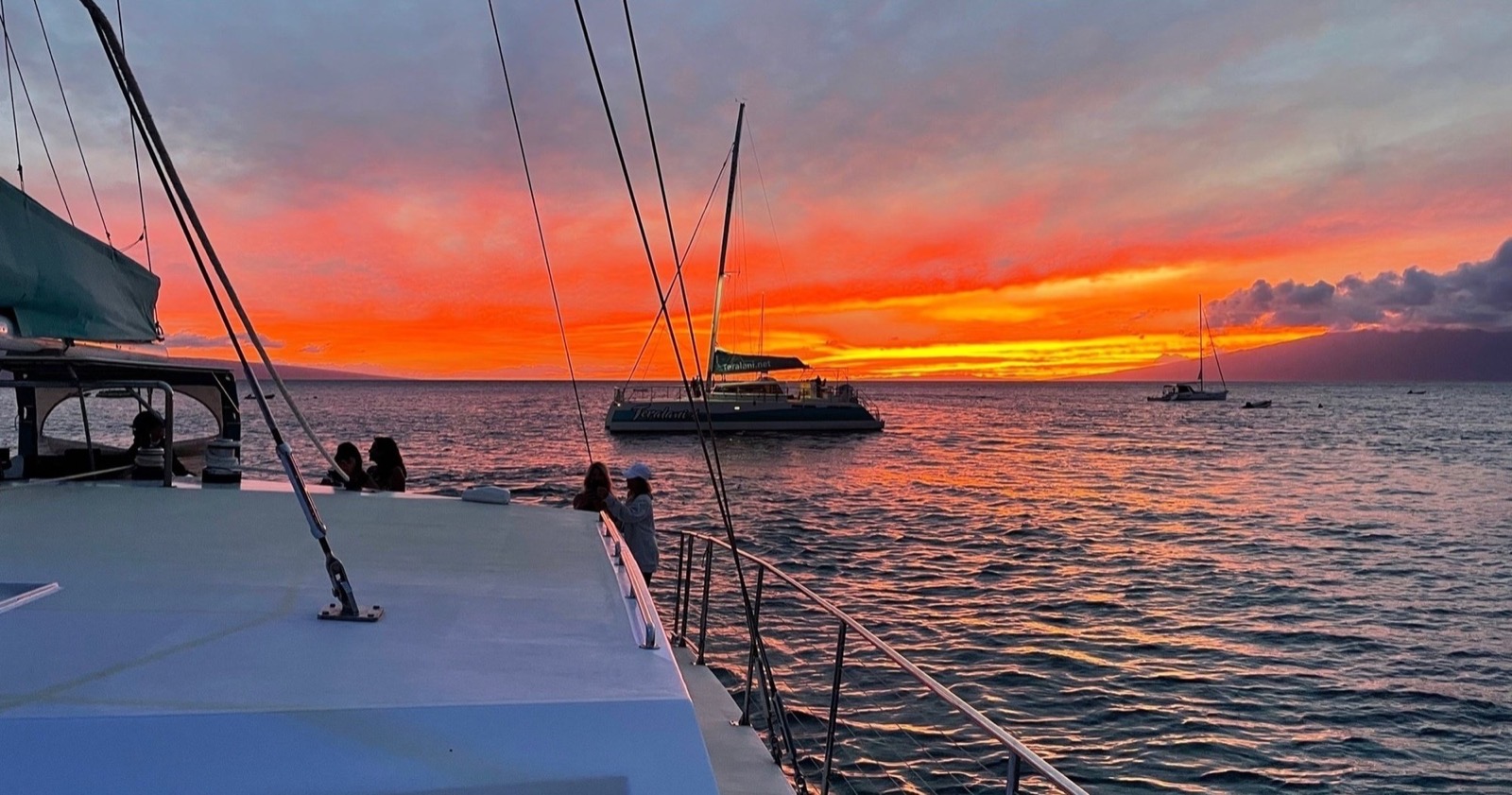 Fiery red and orange sunset with another catamaran silhouetted on the water and guests at the rail