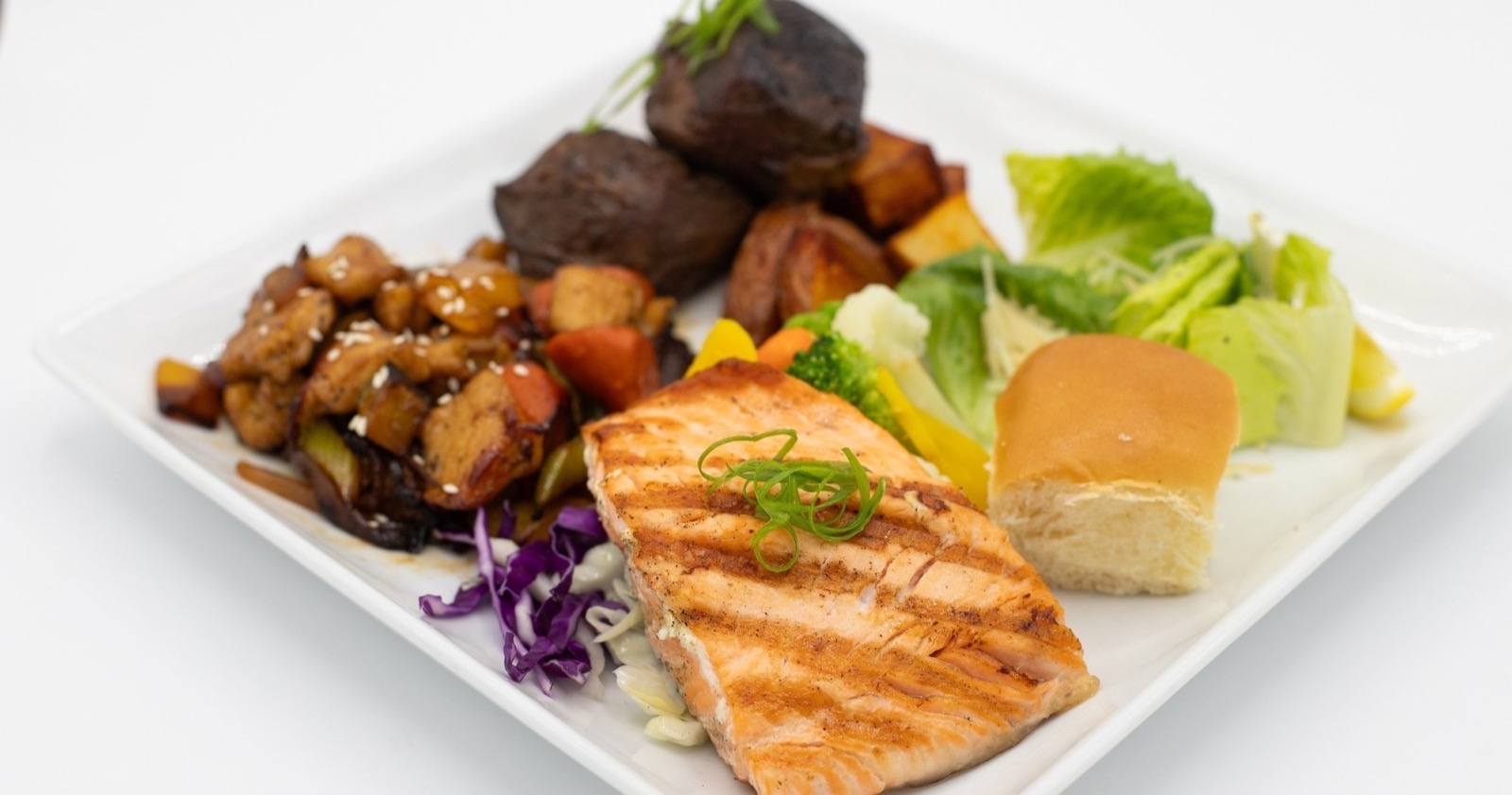 A buffet dinner plate with grilled teriyaki salmon, braised short rib, Kung Pao chicken, vegetables, potatoes, salad and a dinner roll