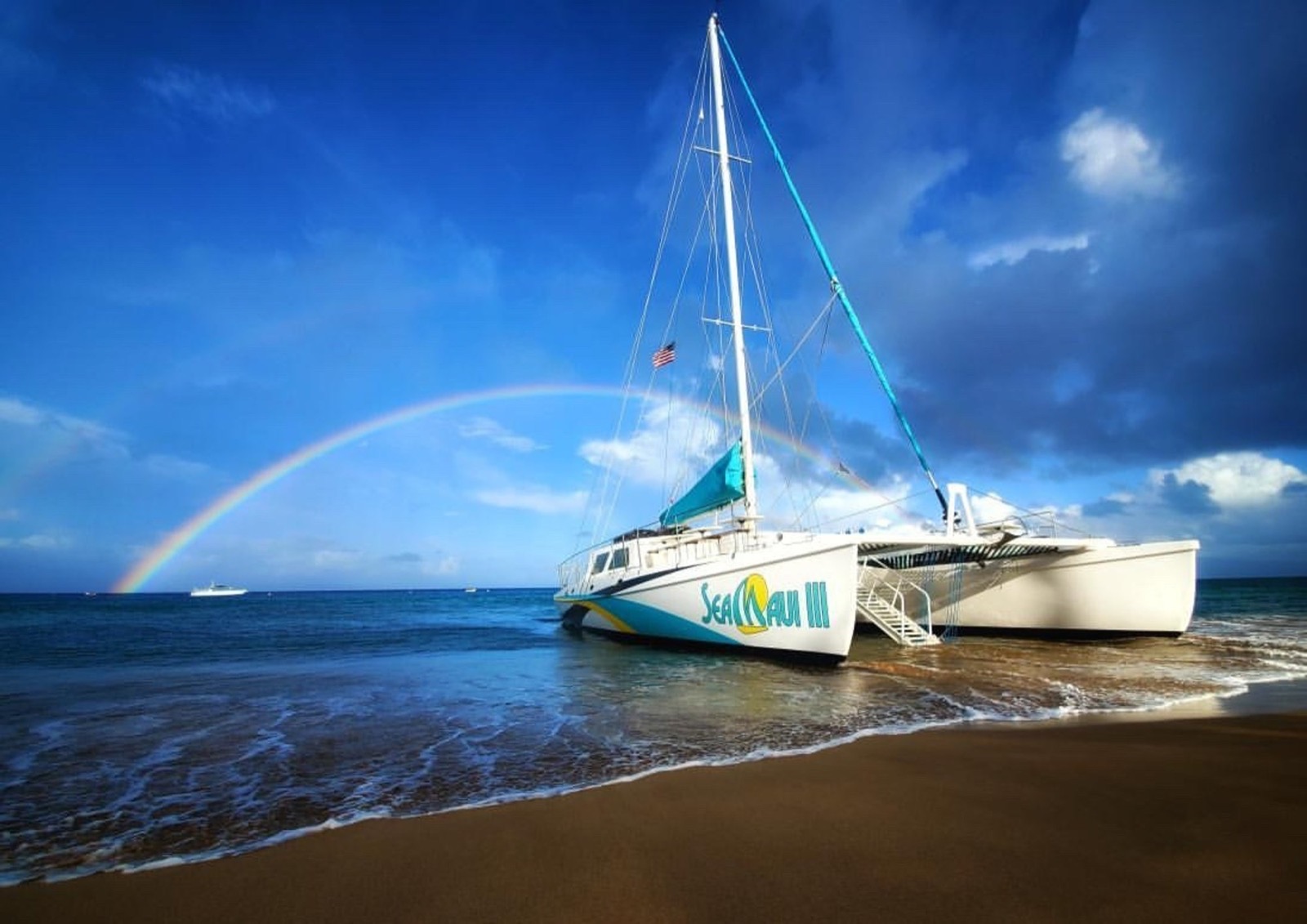 The Sea Maui III catamaran beached on the sand at Kaanapali under a rainbow and deep blue sky