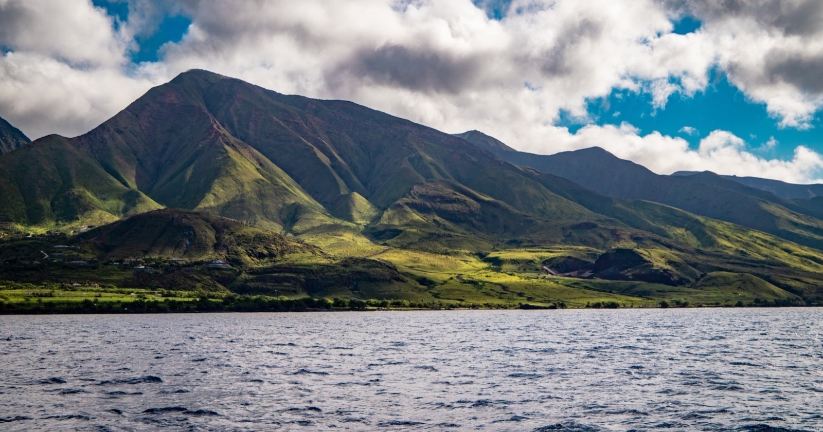 Green slopes of the West Maui Mountains rising above the ocean, seen from the water
