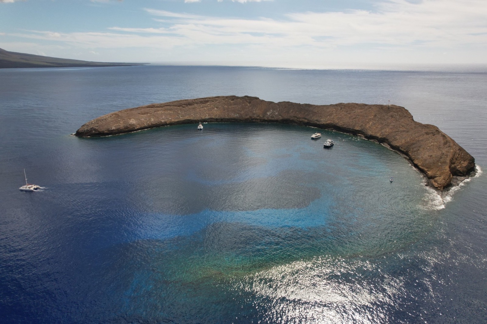Aerial view of the crescent-shaped Molokini islet with a few tour boats anchored inside its sheltered curve