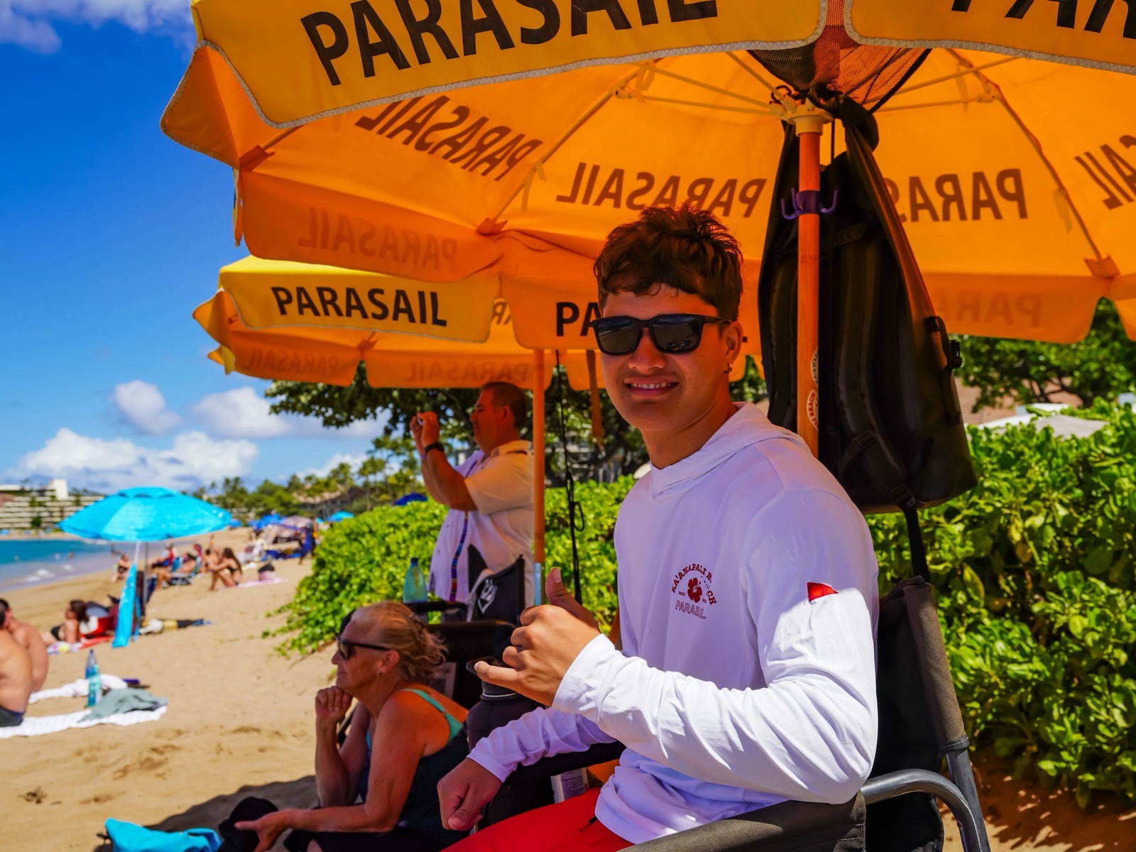 A smiling crew member giving a shaka under a cluster of yellow PARASAIL umbrellas at the check-in spot on Kaanapali Beach